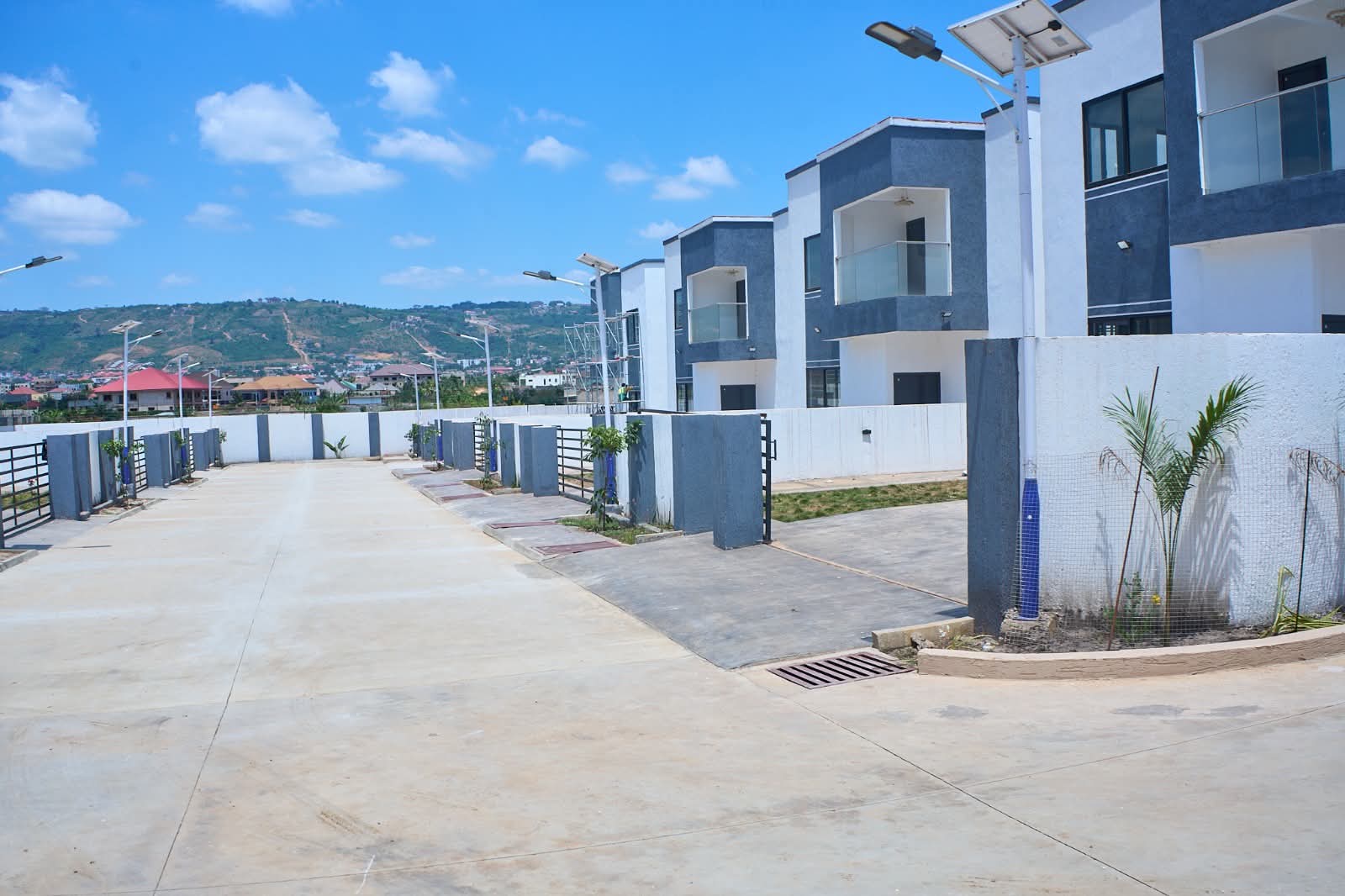 A wide paved street lined with finished homes, with hills beyond